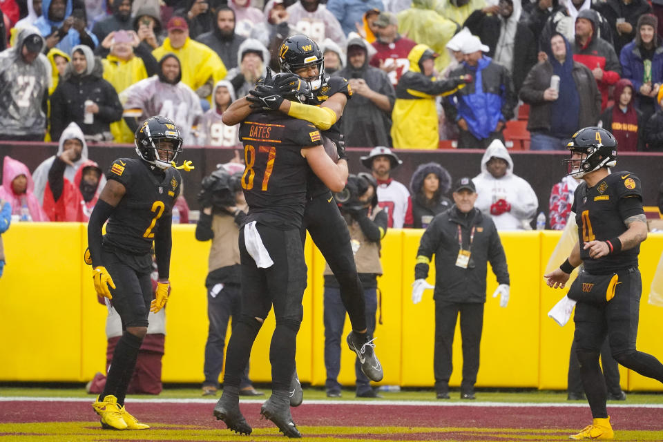 Washington Commanders tight end John Bates (87) is hugged by teammate tight end Logan Thomas (82) after scoring a touchdown against the Atlanta Falcons during the second half of an NFL football game, Sunday, Nov. 27, 2022, in Landover, Md. Also on the field are Washington Commanders wide receiver Dyami Brown (2) and quarterback Taylor Heinicke (4). (AP Photo/Alex Brandon)