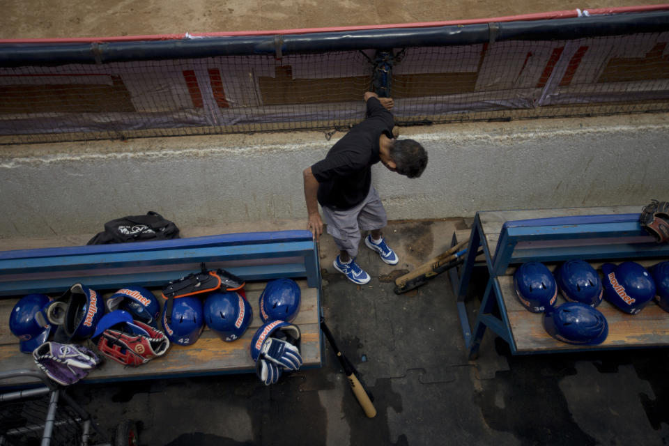 In this Oct. 12, 2018 photo, a stadium worker adjusts floor mats in the dugout of the Tiburones de La Guiara team prior to the baseball season's opening game between Leones de Caracas and Tiburones de la Guaira in Caracas, Venezuela. During the offseason, vandals picked through stadiums across the country; groundskeepers have been battling water shortages; and ticket prices remain a mystery, with most clubs changing them by the week to keep pace with inflation soon reach 10 million percent. (AP Photo/Fernando Llano)