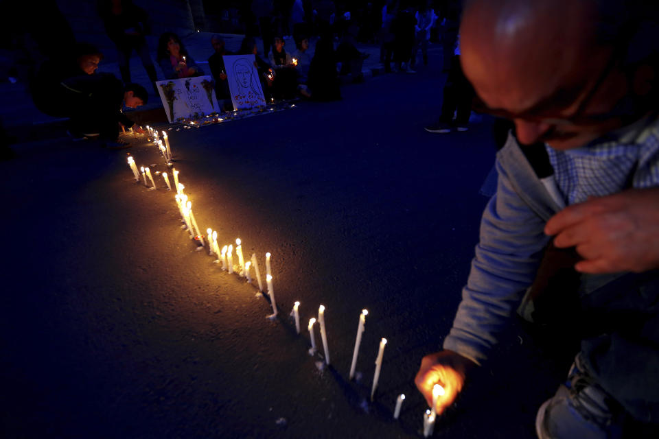 A man lights a candle in memory of victims, outside the presidential palace in capital Nicosia, Cyprus, Friday, April 26, 2019. Up to 1,000 people turned out in front of Cyprus' presidential palace to remember the five foreign women and 2 girls that a military officer has confessed to killing in what police are again calling "an unprecedented crime." (AP Photo/Petros Karadjias)