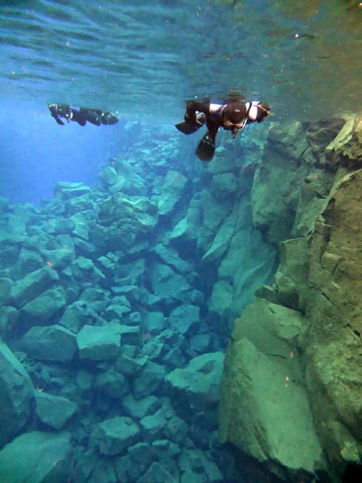 This Jan. 23, 2013 photo provided by the diving excursion company DIVE.IS shows snorkelers traversing Iceland’s Silfra, a rift fed by glacier water. Because of its pure water and stunning colors, Silfra has become a popular site for divers despite near-freezing temperatures. (AP Photo/DIVE.IS, Louis Kotze)