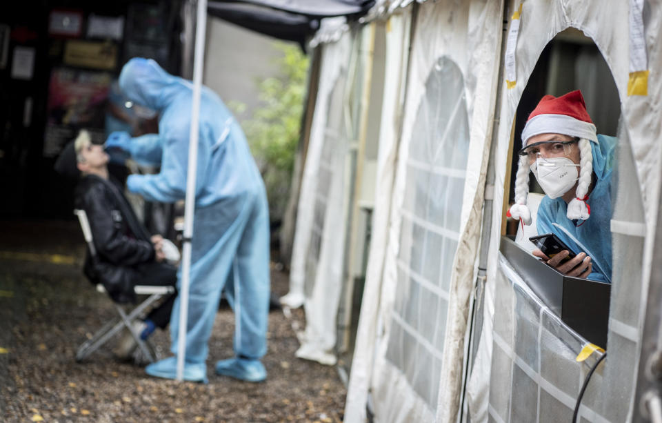 An employee of the Corona Test Center at the night club 'Kitkat Club' looks out of the tent with a Santa hat while a Corona rapid test is taken in the background in Berlin, Germany, Tuesday, Dec. 22, 2020. (Kay Nietfeld/dpa via AP)