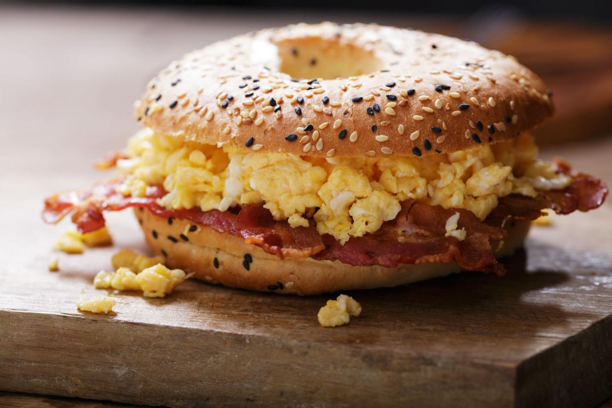 Breakfast sandwich with bagel, scrambled eggs, bacon and cheese on wooden board