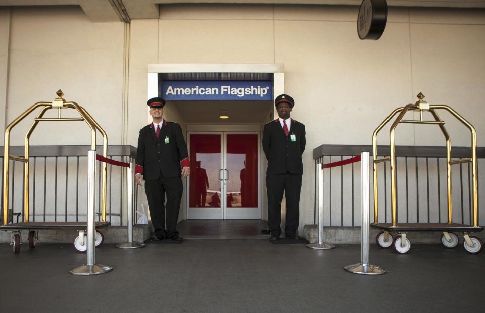 FILE - In this Thursday, March 14, 2013 file photo, American Airlines skycaps Alex Abel Gonzalez, left, and Frederick Pearson await outside the AA Flagship lounge at Los Angeles International Airport, LAX. American's Flagship Check-in service, a VIP discreet and expedited check-in process offers personal access to agents for assistance with check-in and bag check, and a separate security line when flying through several large American airports. (AP Photo/Damian Dovarganes, File)