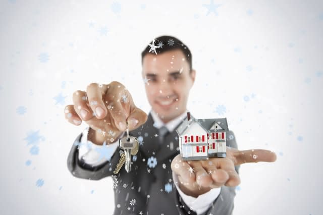 Close up of keys and miniature house being held by male estate agent against snow falling