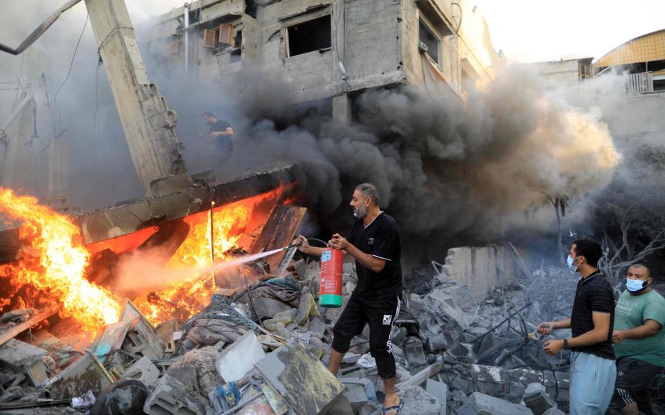 A Palestinian man uses a fire extinguisher to douse a fire following an Israeli strike, in Khan Yunis in the southern Gaza Strip on October 14, 2023.