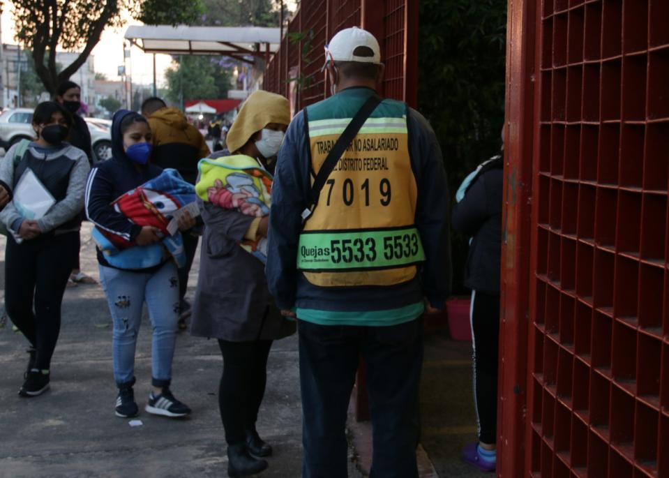 Masked people stand in line outside a hospital with their babies.