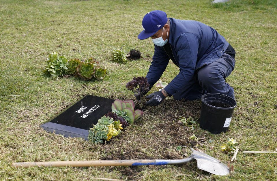 Francisco Ventura, an employee at Hollywood Forever cemetery, places flowers around a temporary headstone for the late actor Burt Reynolds in the Garden of Legends section of the cemetery, Thursday, Feb. 11, 2021, in Los Angeles. Reynolds' cremated remains were moved from Florida to Hollywood Forever, where a small ceremony was held Thursday. A permanent gravesite will be put up for Reynolds in a few months. (AP Photo/Chris Pizzello)