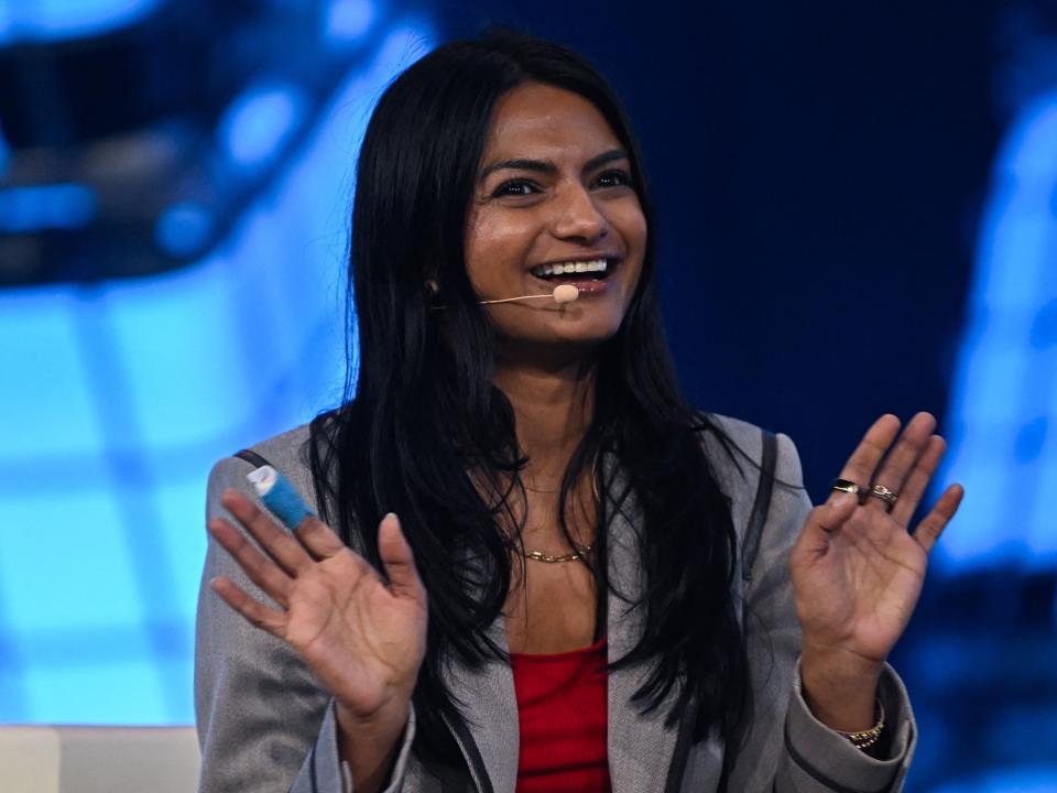 Foto del CEO de Only Fans, Ami Kahn, con un blazer y una falda go-art grises y un top rojo al micrófono en el escenario en Web Summit Rio