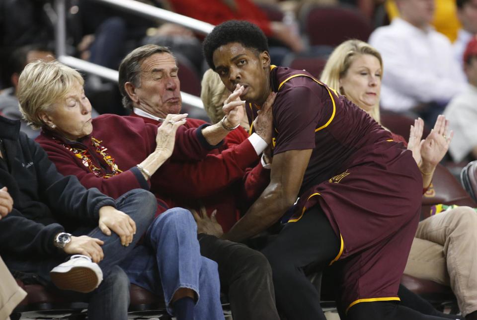 FILE - In this Jan. 9, 2014 file photo, Arizona State's Shaquielle McKissic runs into spectators sitting in courtside seats as he tries to prevent a ball from going out of bounds against Southern California during the second half of an NCAA college basketball game in Los Angeles. Oklahoma State All-American guard Marcus Smart is serving a three-game suspension for shoving a fan who later apologized for his actions. The incident shows how volatile the interaction between fans and athletes is becoming. (AP Photo/Danny Moloshok, File)