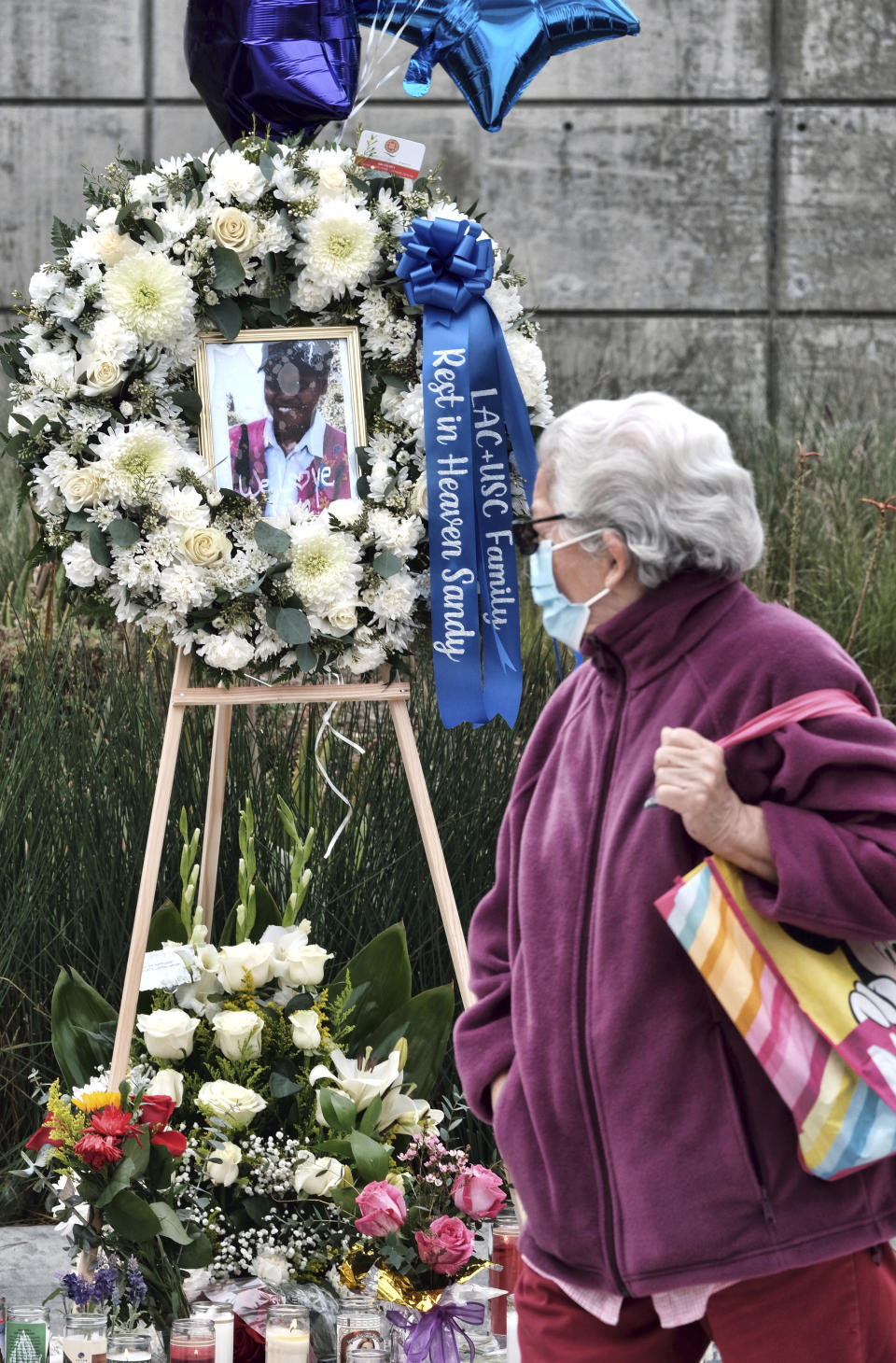 A commuter glances at a memorial for Nurse Sandra Shells at the bus stop on Wednesday, Jan. 19, 2022 in downtown Los Angeles where Shells had been attacked last Thursday. Shells, a 70-year-old nurse, was on her way to work at LA County-USC Medical Center when she was allegedly stabbed, fell backward and hit her head on the ground. She died Sunday, Jan. 16, 2022 at a hospital. (AP Photo/Richard Vogel)