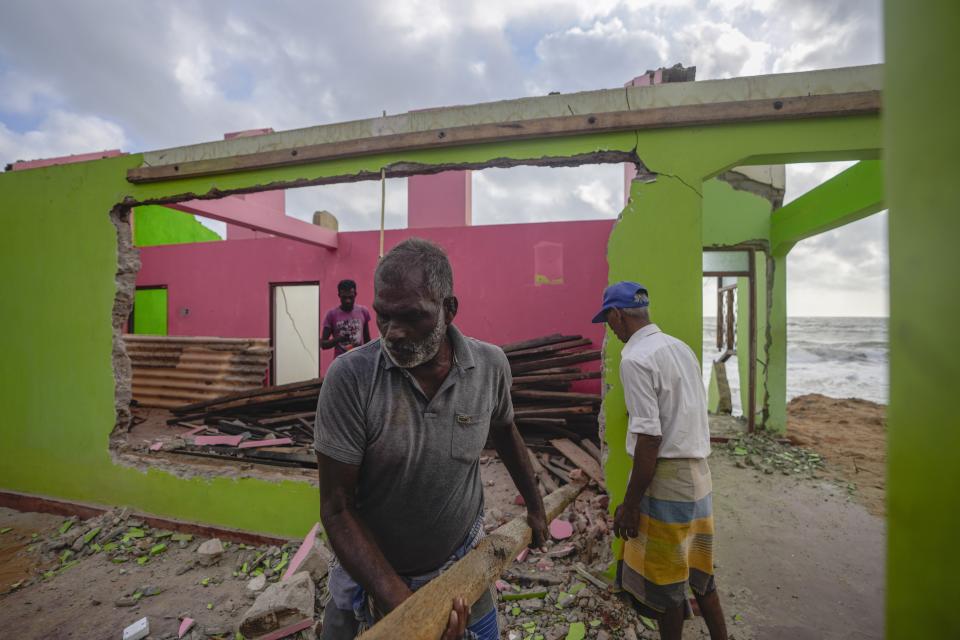 Ranjit Sunimal Fernando, front, salvages reusable rafters from the wreck of his home destroyed by erosion in Iranawila, Sri Lanka, Thursday, June 15, 2023. Much like the hundreds of other fishing hamlets that dot the coastline, the village of Iranawila suffers from coastal erosion. (AP Photo/Eranga Jayawardena)