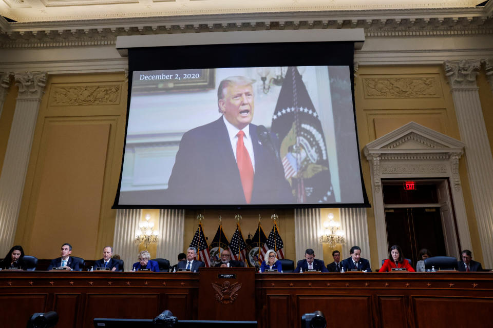 Former President Donald Trump appears on a large screen above the assembled members of the panel.