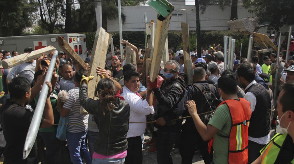 Volunteers bring pieces of wood to help prop up sections of the collapsed school. Source: AP