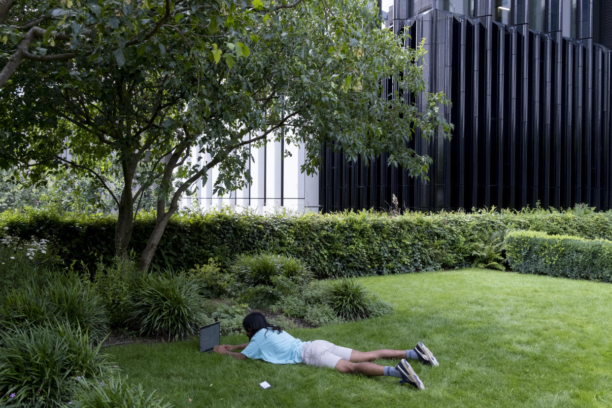 A man lies on the grass beneath largely empty office premises in London on July 21, 2021. (Photo by Richard Baker / In Pictures via Getty Images)