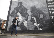 Loyalist activist Jamie Bryson walks past a Ulster Volunteer Force mural in east Belfast, Northern Ireland, Tuesday, Oct. 15, 2019. Fears about a return to the violence that killed more than 3,500 people over three decades have made Northern Ireland the biggest hurdle for U.K. and European Union negotiators trying to hammer out an agreement on Britain's departure from the 28-nation free trade bloc. People here are worried that UK Prime Minister Boris Johnson will sacrifice their interests in hopes of securing a deal. Anything that treats Northern Ireland differently than the rest of the U.K. would be unacceptable. "There would be an organic explosion of anger and people would take to the streets and obviously any sensible person would be urging people ... to do so peacefully,'' said Jamie Bryson, editor of the Unionist Voice newsletter, as he offered an analysis of where the community stands. (AP Photo/Peter Morrison)