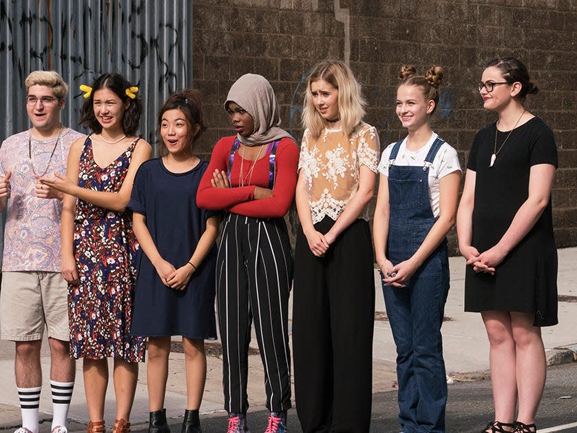 Line of contestants on "Project Runway: Junior" as they listen to guidelines for a competition. The writer stands on far right and wears a black dress