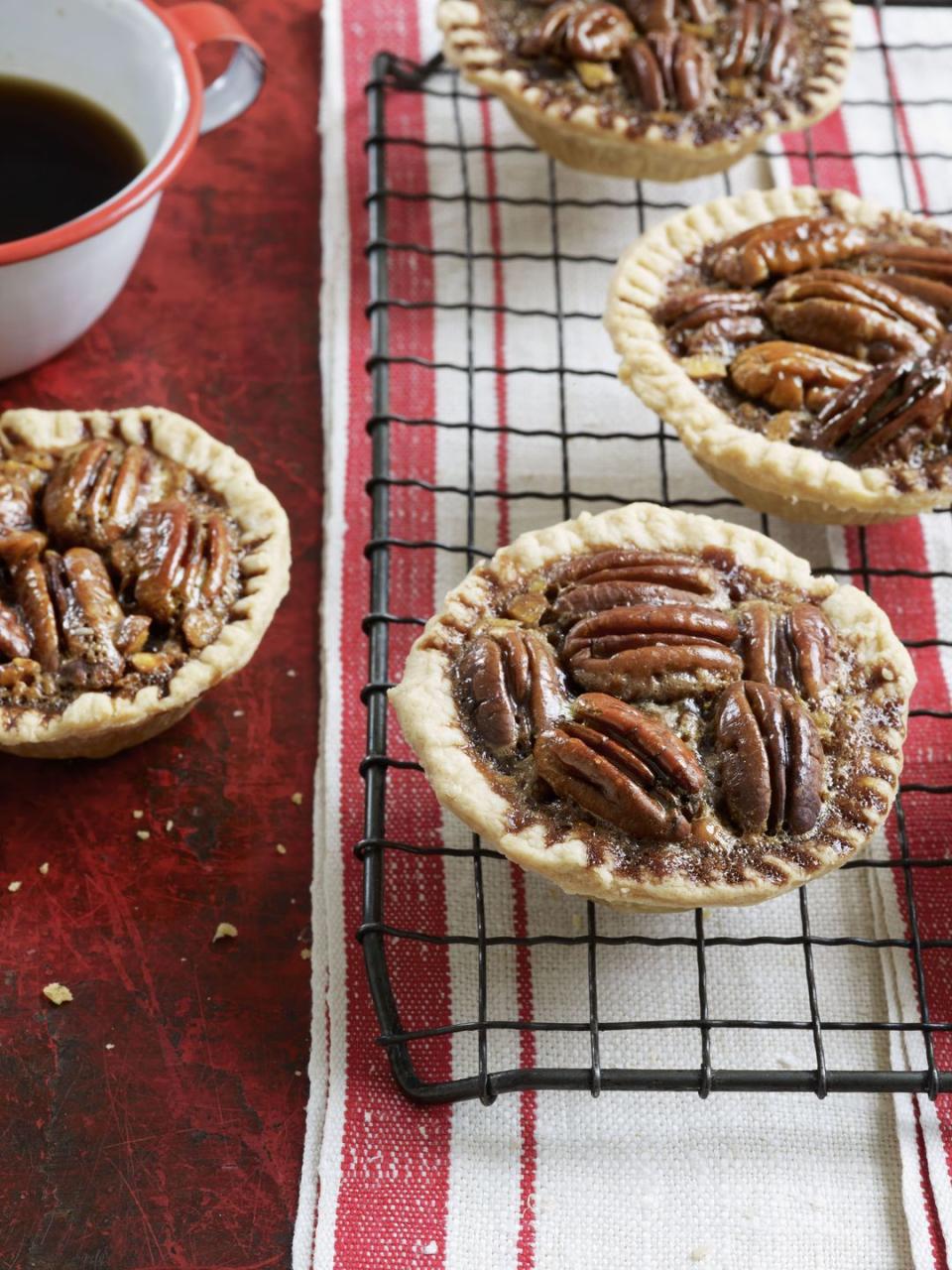 mini chocolate pecan tartlets on a wire rack over a red and white striped kitchen towel