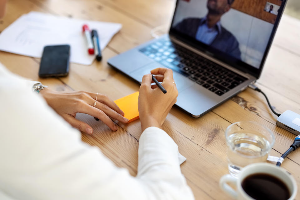 Close-up of a female executive sitting at her office desk making a video call with laptop computer. Businesswoman having a video conference and taking notes.