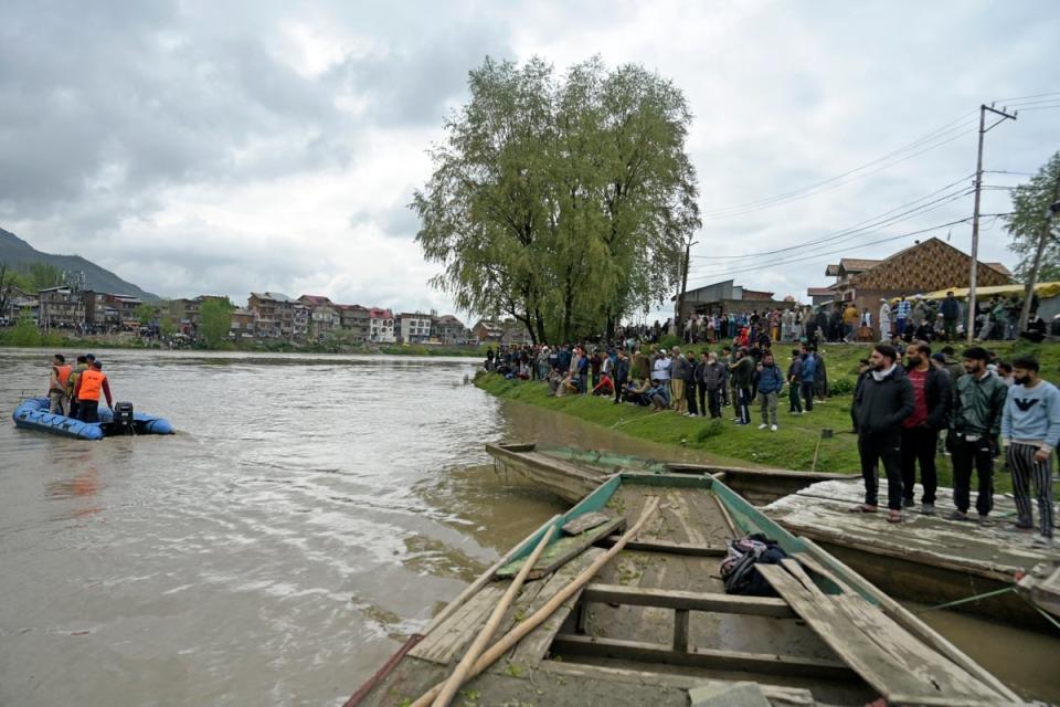 People gather along the bank of the Jhelum river as National Disaster Response Force (NDRF) personnel (L) conduct a rescue and search operation after a boat ferrying people capsized in Srinagar (AFP via Getty Images)