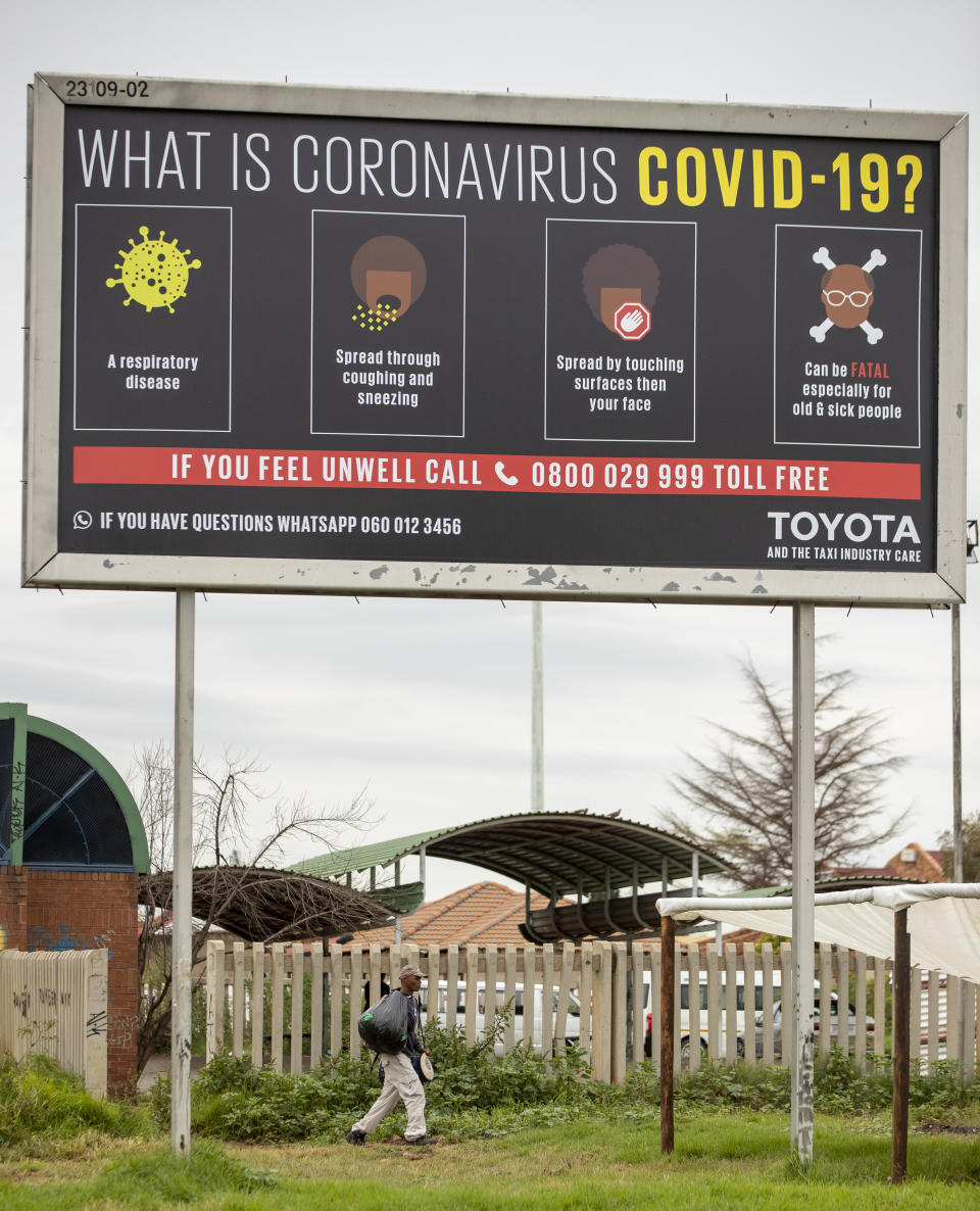 A man carrying recycling materials walks under a billboard explaining coronavirus in Vosloorus, east of Johannesburg, South Africa, Thursday, April 2, 2020. South Africa went into a nationwide lockdown for 21 days in an effort to mitigate the spread to the coronavirus. The new coronavirus causes mild or moderate symptoms for most people, but for some, especially older adults and people with existing health problems, it can cause more severe illness or death. (AP Photo/Themba Hadebe)