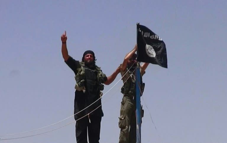 An image made available by the jihadist Twitter account Al-Baraka news on June 11, 2014 allegedly shows militants of the jihadist group Islamic State hanging their flag on a pole at a site on the Syrian-Iraqi border