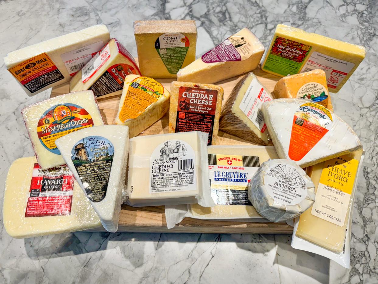 Bird's-eye-view of 17 blocks of Trader Joe's cheese on a wooden cutting board placed on a gray counter