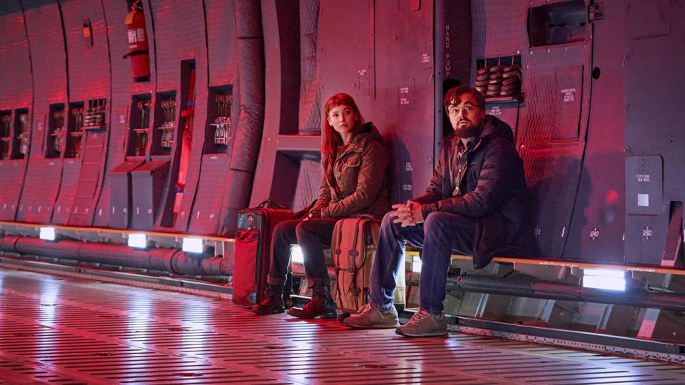 A woman and a man sit on a bench in a long hallway in this still from the movie Don't Look Up