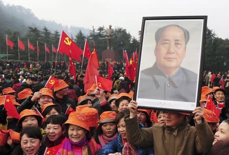 A man holds up a portrait of the late Chairman Mao Zedong as he and others gather in front of a giant statue of Mao on a square to celebrate the 120th birth anniversary of the former leader, in Shaoshan, Mao's hometown, December 26, 2013. REUTERS/Stringer