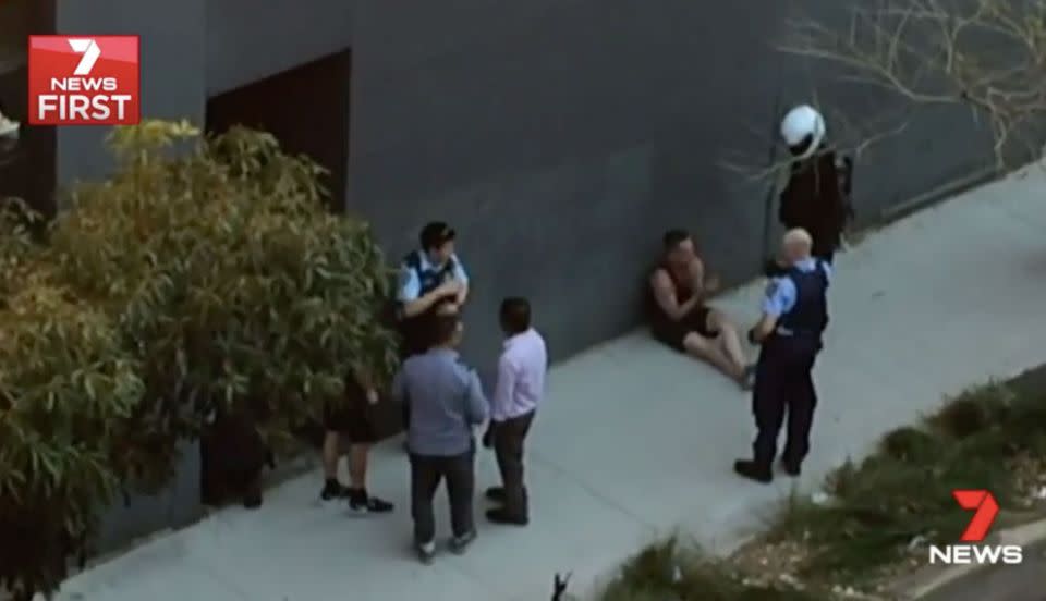 The man appears to be handcuffed and sits up, under arrest. Source: 7 News