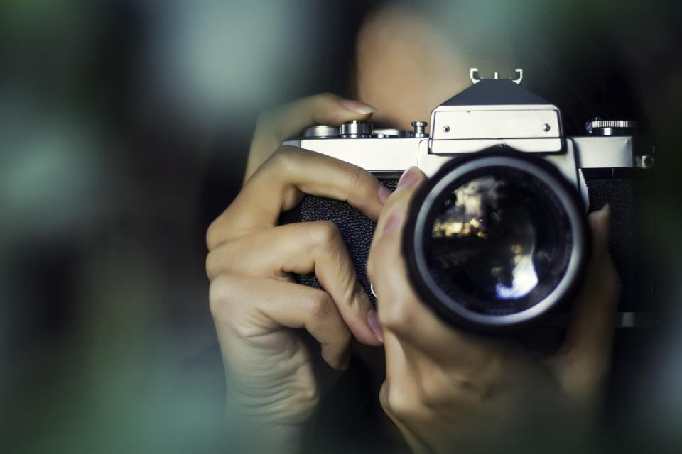 A person holding and looking through a camera, with their face mostly obscured by the camera