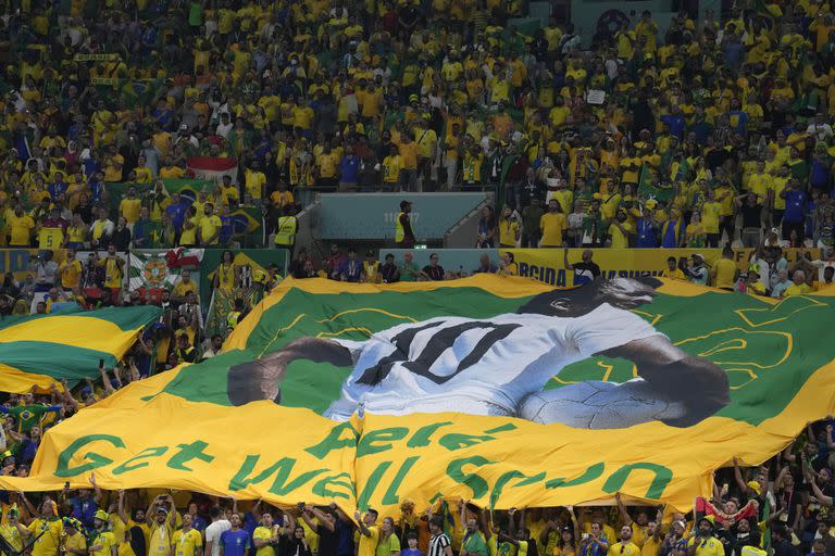 Fanáticos brasileños extienden una bandera brasileña gigante con la imagen del exastro brasileño Pelé con un mensaje que dice en inglés "Pelé. Recupérate pronto", durante el partido entre la selección verde amarela y Camerún, dentro del Grupo G de la Copa del Mundo, en el estadio en Lusail, en Qatar, el viernes 2 de diciembre de 2022. (AP Foto/Natacha Pisarenko) :