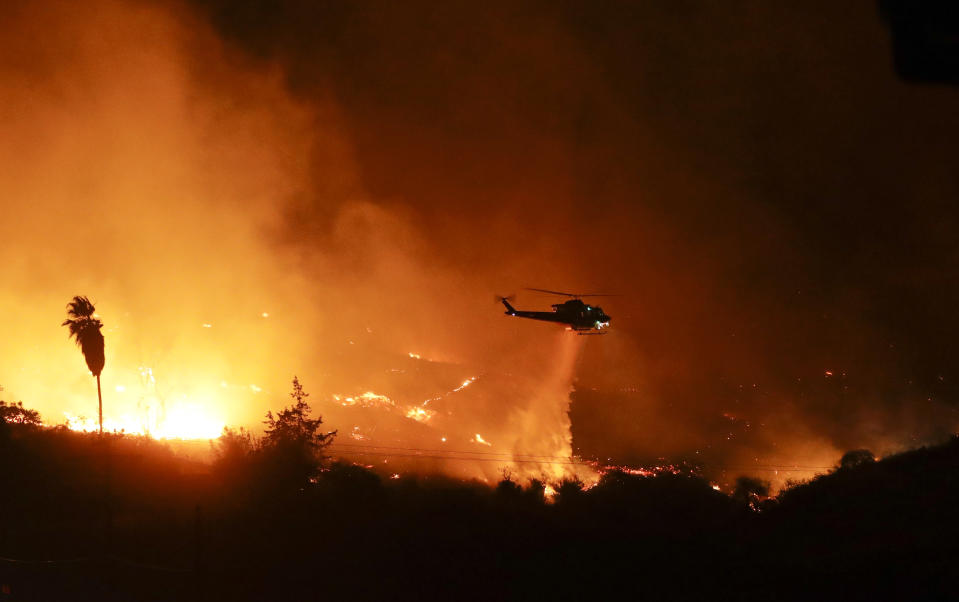 FILE - A helicopter drops water over a wildfire, Dec. 7, 2017, in Bonsall, Calif., that forced evacuations. Environmental groups have been arguing in California courts that developers are not fully considering the risks of wildfire and choked evacuation routes when they plan housing developments near fire-prone areas. (AP Photo/Gregory Bull, File)