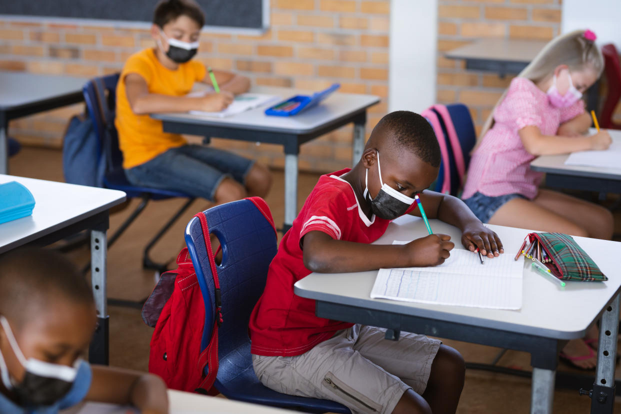 African American boy wearing face mask studying while sitting on his desk in the class at school. The CDC guidance recommended that everyone in K-12 schools wear a mask indoors.