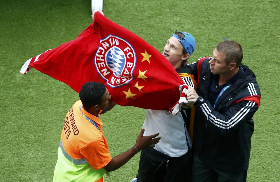 Stewards escort a Germany fan waving a Bayern Munich towel off the pitch during the team's 2014 World Cup Group G soccer match against the U.S. at the Pernambuco arena in Recife June 26, 2014.REUTERS/Ruben Sprich (BRAZIL - Tags: SOCCER SPORT WORLD CUP)