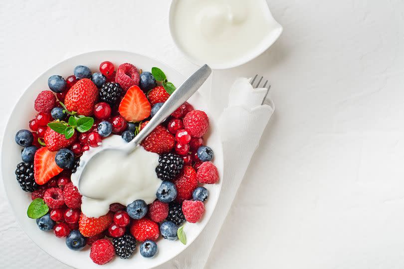 Bowl of healthy fresh berry fruit meal with cream on white background. Top view. Berries overhead closeup colorful assorted mix of strawberry, blueberry, raspberry, blackberry, red currant