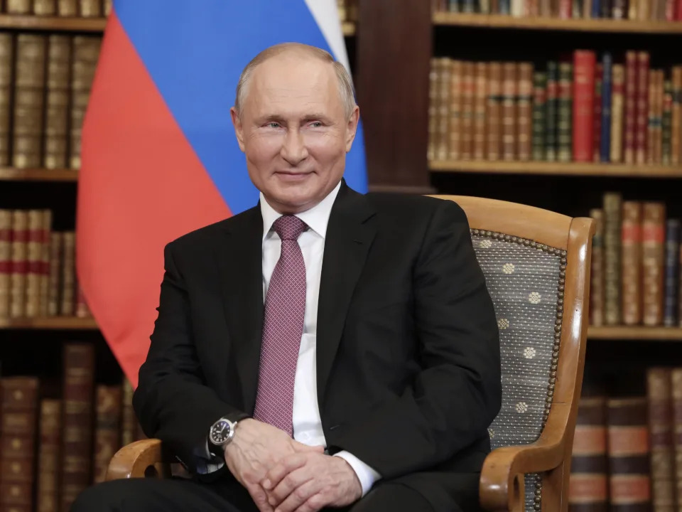 Vladimir Putin sits and smiles.