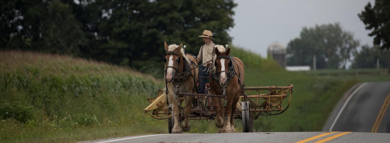 An Amish teen pulls farm machinery down a road in La Farge.