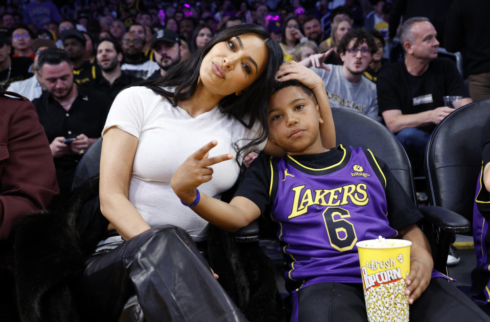 Kim Kardashian and Saint West sit courtside at a basketball game. Kim is dressed casually, and Saint wears a Lakers jersey, holding popcorn