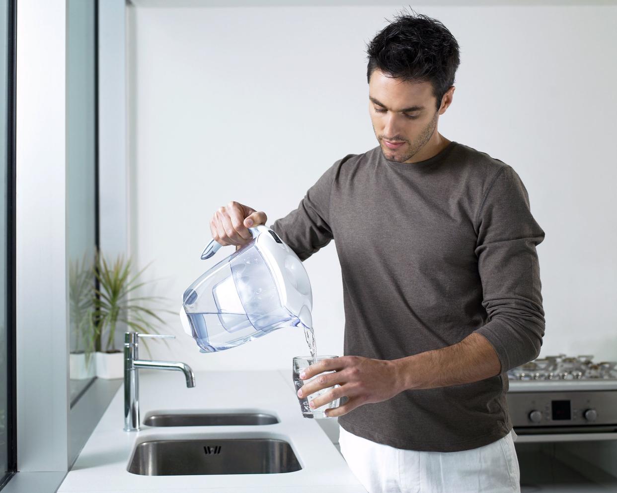 man pouring water from water filter pitcher into glass