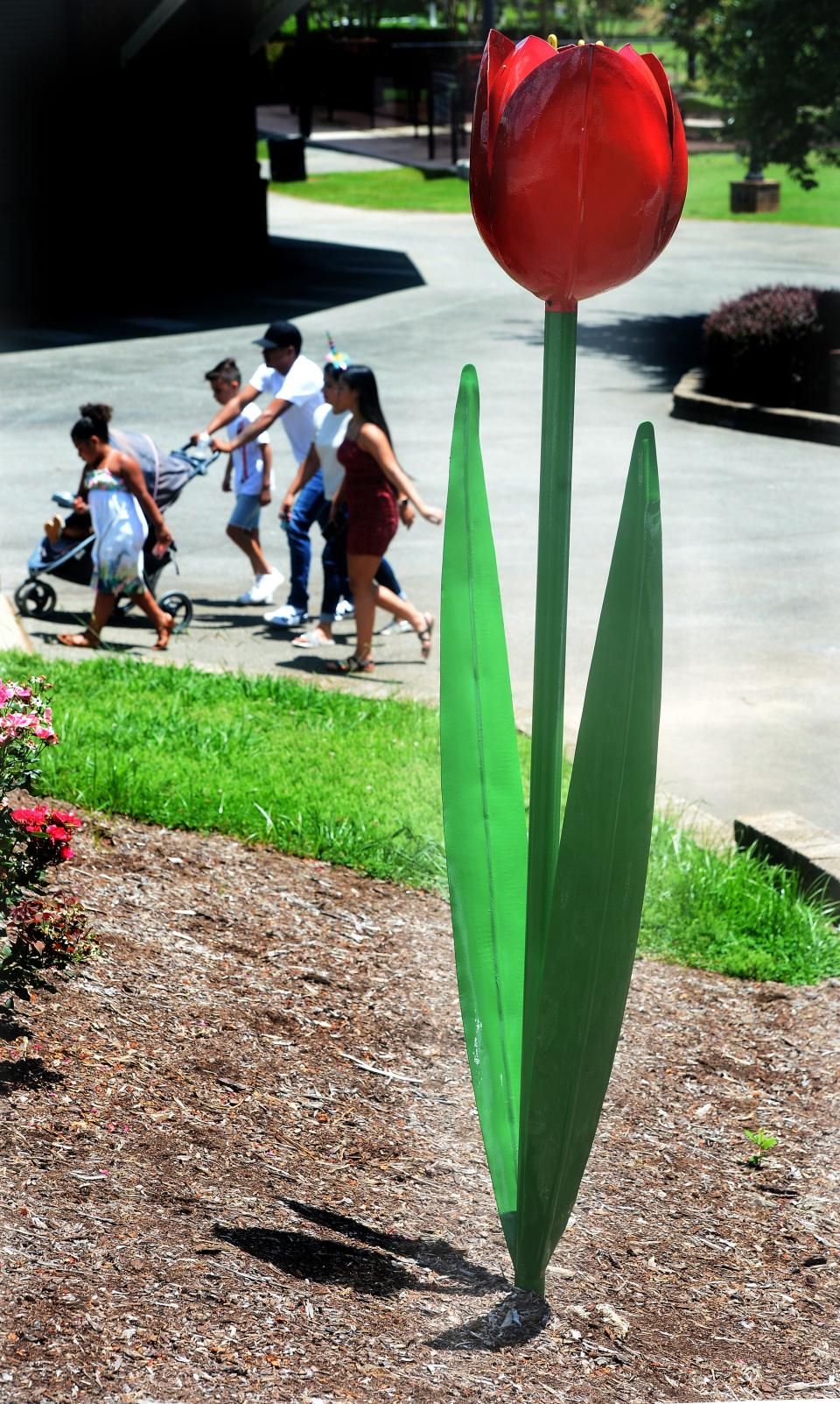 A family walks by the tulip sculpture by Casey Lewis on display at Burlington City Park.