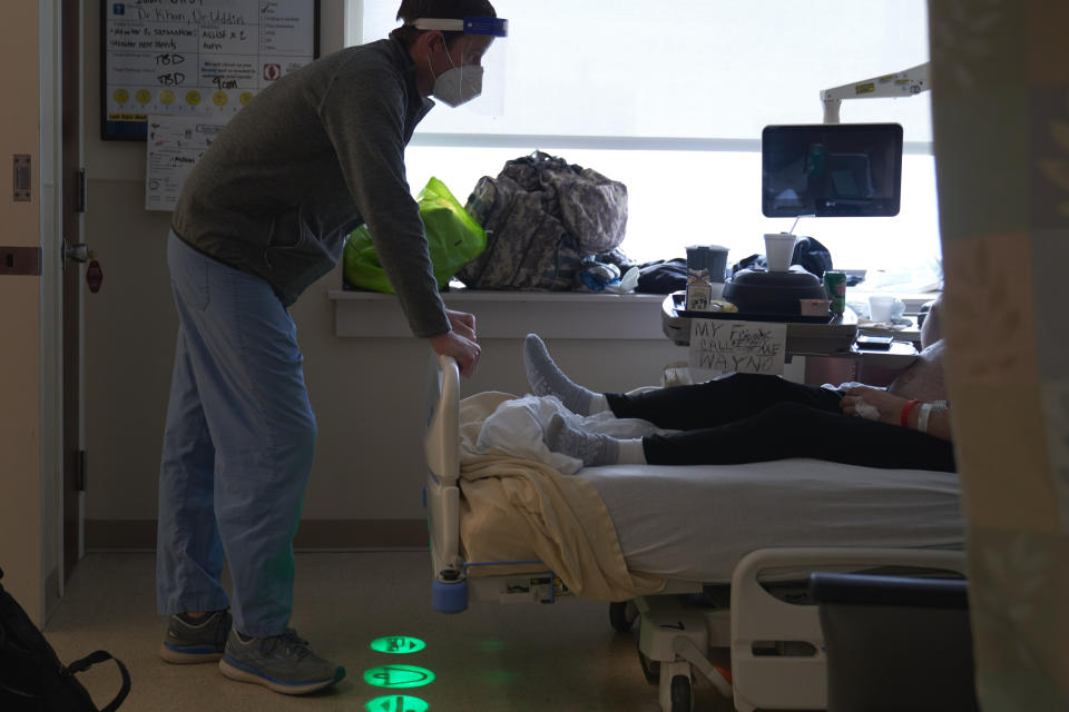 A doctor wearing a mask leans over the foot of a hospital bed as he speaks with an unvaccinated Covid patient. 