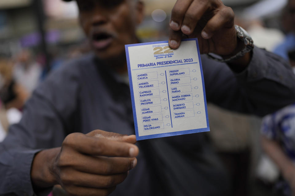 A man explains how to vote while holding up an unmarked ballot as he opens a polling station for the opposition's primary presidential election at Luis Brion square in Caracas, Venezuela, Sunday, Oct. 22, 2023. The opposition will pick one candidate to challenge President Nicolás Maduro in 2024 presidential elections. (AP Photo/Matias Delacroix)