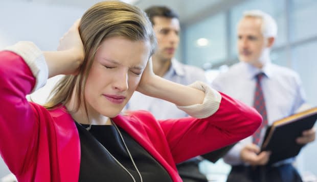 Female executive looking frustrated in an office with her colleagues discussing in the background