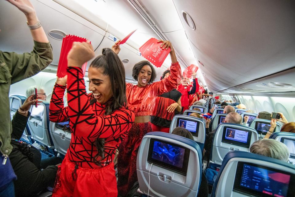 Virgin Voyages crew members wearing red dance through an aircraft cabin