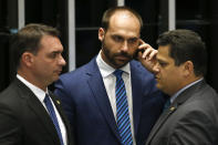 Senate President Davi Alcolumbre, right, talks with lawmaker Eduardo Bolsonaro, center, and Senator Flavio Bolsonaro, both sons of the nation's president, during the final voting session on pension reform at the Senate in Brasilia, Brazil, Tuesday, Oct. 22, 2019. The most meaningful impact is the establishment of a minimum age for retirement at 65 for men and 62 for women. (AP Photo/Eraldo Peres)