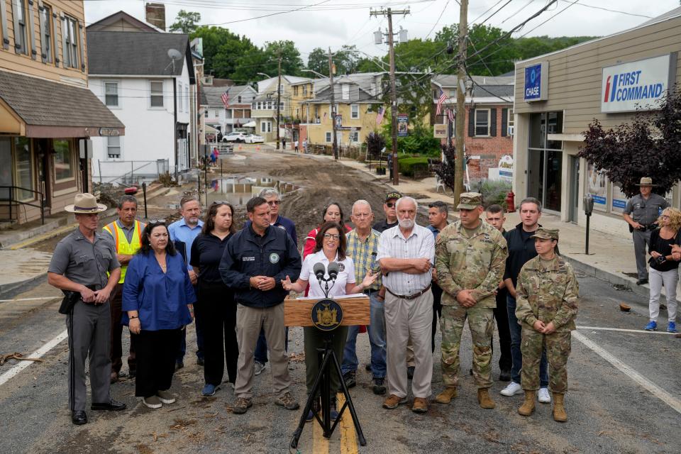 New York Gov. Kathy Hochul, center, alongside an entourage of emergency workers and officials, speaks to members of the media on Main Street damaged the previous day by floodwaters, Monday, July 10, 2023, in Highland Falls, N.Y. (AP Photo/John Minchillo)