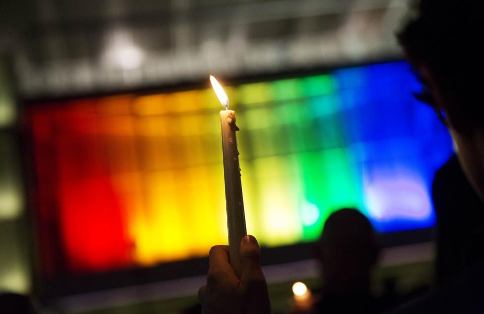 <p>A mourner holds up candle against a rainbow-lit backdrop during a vigil on Monday, June 13, 2016, for those killed in a mass shooting at the Pulse nightclub in downtown Orlando, Fla. (Photo: David Goldman/Associated Press) </p>