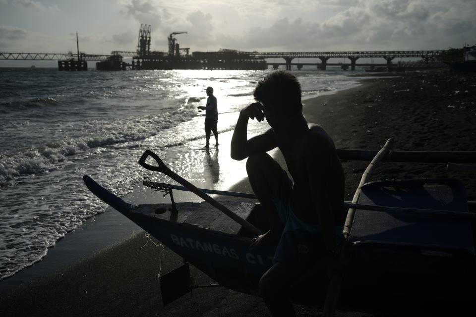 A resident fishes as the sun sets at the coastal village of Santa Clara near a liquefied natural gas power plant in Batangas province, Philippines on Tuesday, Aug. 8, 2023. The Philippines is seeing one of the world's biggest buildouts of natural gas infrastructure. (AP Photo/Aaron Favila)