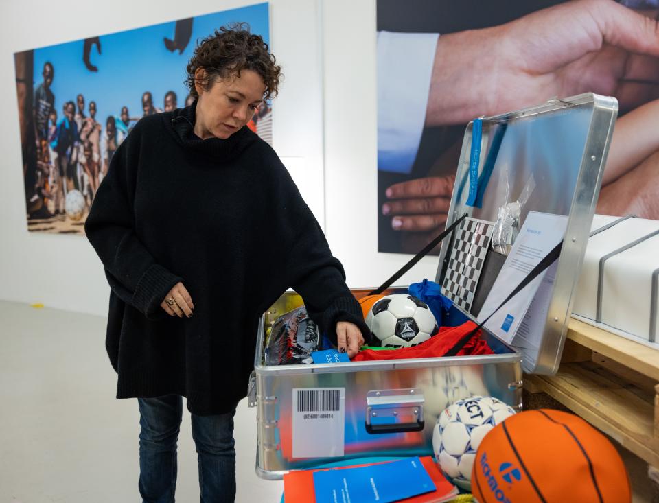 Olivia Colman standing next to a box full of supplies 