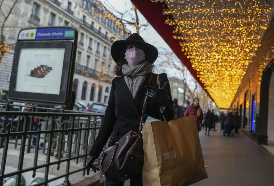 A woman wearing face mask to protect against COVID-19 walks with a shopping bag along a shopping center in Paris, Friday, Dec. 17, 2021. France's government is desperately trying to avoid a new lockdown or stricter measures that would hurt the economy and cloud President Emmanuel Macron's expected campaign for the April presidential election. (AP Photo/Michel Euler)